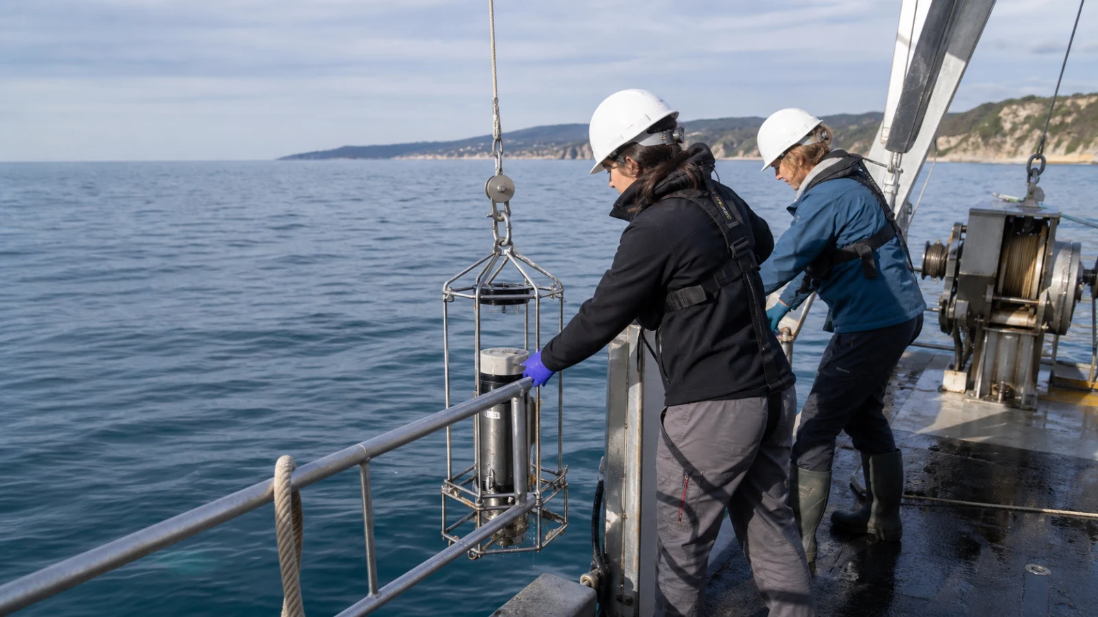 Scientists lowering a marine water sampling frame from a research vessel